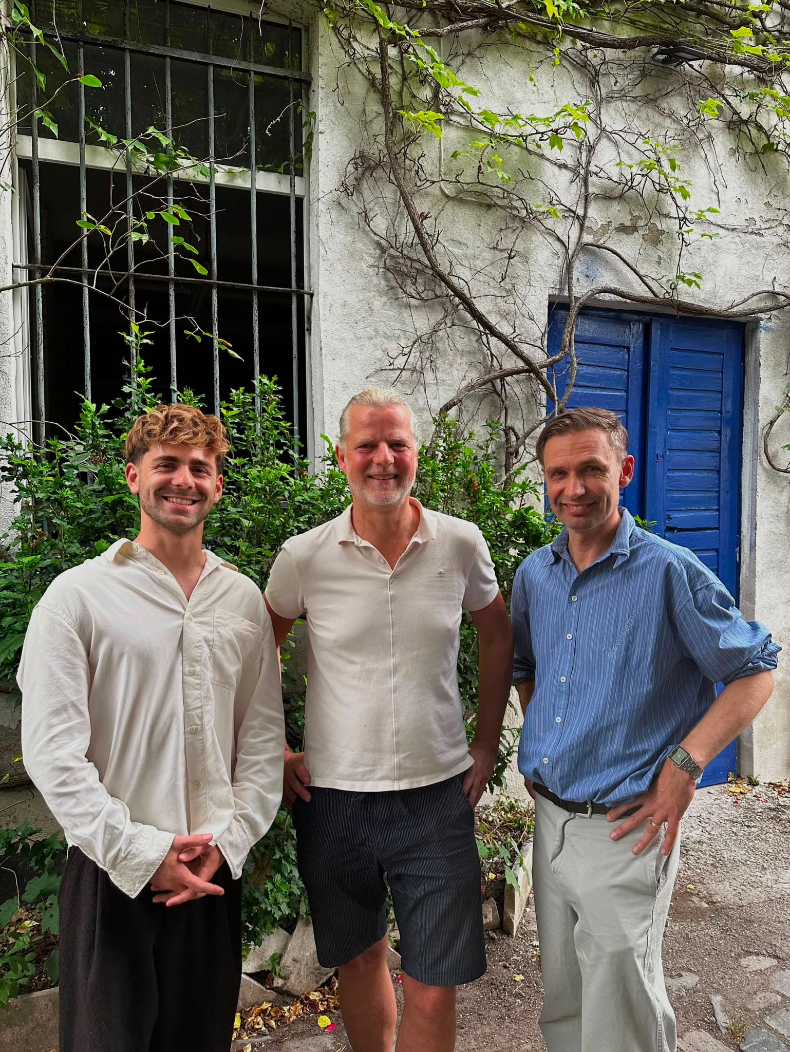 Das Team der Rosenhöfe gemeinsam im begrünten Innenhof vor einer mediterran-blauen Tür
